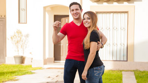 Young couple posing with house keys in front of new house